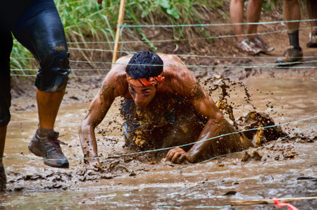 Dallas, USA - September 15, 2012 - Mud race participant crawling through a mud pit. Dash of the Titans Dallas Texas Mud Run Race.のeditorial素材