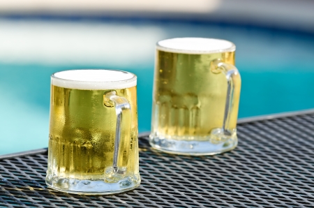 Two cold beer glasses on the table by blue swimming pool on a sunny summer dayの写真素材