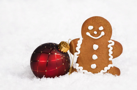 Gingerbread man cookie and red Christmas ball ornament on snow の写真素材