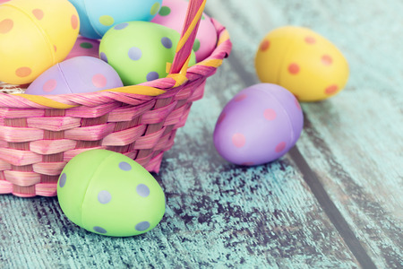 Pink Easter basket with pastel colored eggs on vintage green wooden background