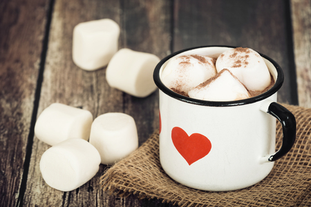 Hot chocolate and marshmallows in old enamel cup with heart. Rustic wooden background.の写真素材
