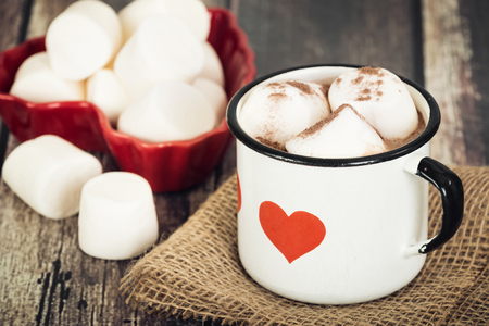 Hot chocolate and marshmallows in old enamel cup with heart. Rustic wooden background.の写真素材