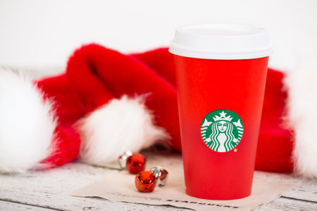 DALLAS, TX - NOVEMBER 10, 2015: A cup of Starbucks popular holiday beverage, served in the new 2015 designed red holiday cup. Displayed with Christmas hats and bells on white rustic table.のeditorial素材