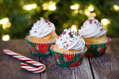 Christmas cupcakes with red and green sprinkles on rustic table. Shallow depth of field. Sparkling Christmas tree lights background.の写真素材