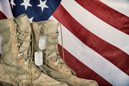 Old combat boots and dog tags with American flag in the background. Vintage filter effects.の写真素材