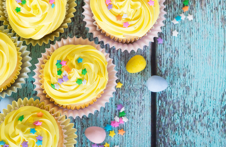 Yellow Easter cupcakes with candy and sprinkles on vintage wooden table. Top view.の写真素材