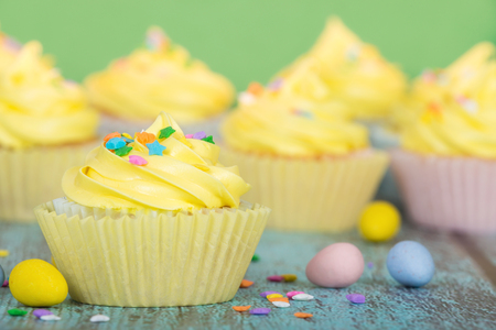 Yellow Easter cupcakes with candy and sprinkles. Green background.の写真素材