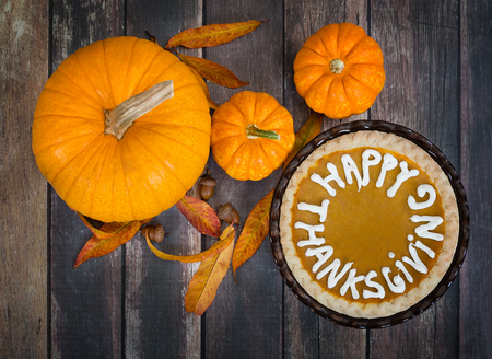 Pumpkin pie with Happy Thanksgiving text. Displayed with pumpkins, golden autumn leaves, and acorns on rustic table. Top view.の写真素材