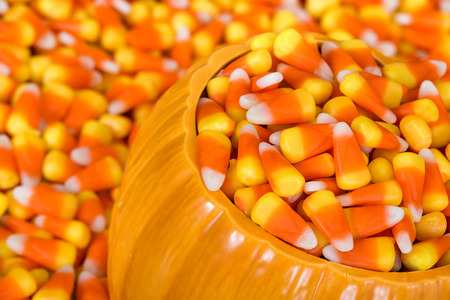 Ceramic decorative pumpkin filled with Halloween candy corn. Closeup with candy corn background.