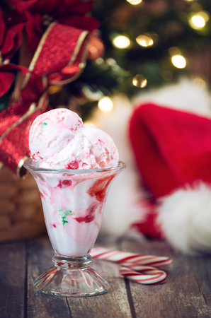 Peppermint ice cream served in a glass bowl. Displayed with candy canes on wooden rustic table. Christmas hat and tree lights background.の写真素材