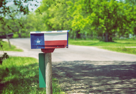 Mailbox painted with a Texas flag along a country road. Lush green trees in the background.の写真素材