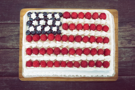Patriotic, red white and blue, American flag cake, decorated with fresh blueberries and raspberries. Top view against rustic wooden background.の写真素材