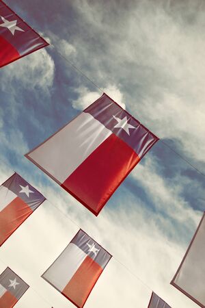 A group of Texas flags hanging against blue sky and white clouds. Vintage filter effects.の写真素材