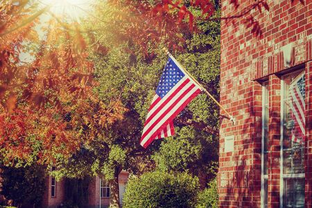 Patriotic American flag waving in front of a brick home on a sunny autumn day. Vintage filter effects.の写真素材