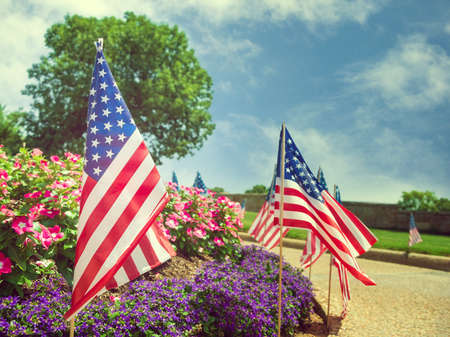 American flags displayed on the side of the street in honor of the 4th of July. Beautiful flower bed and blue sky background.の写真素材