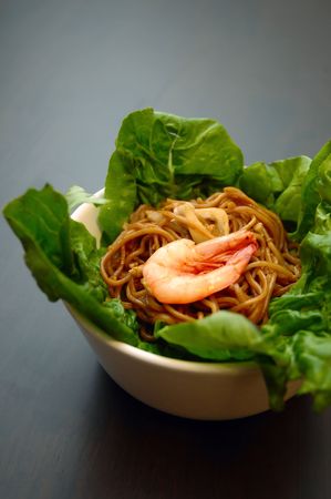 Braised egg noodles with seafood, garnished with shrimp on a bed of romaine lettuce.