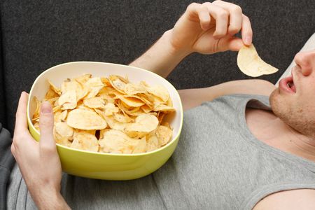 A man on a couch eating potato chipsの写真素材