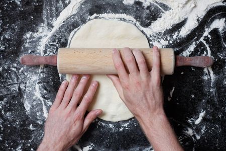 A rolling pin flattening a pizza