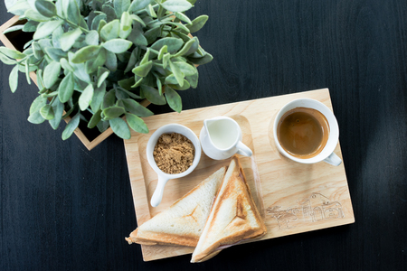 breakfast - coffee, milk, brown sugar and toast with leaves on black backgroundの写真素材