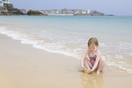 Young girl sitting on beach playing with sandの写真素材