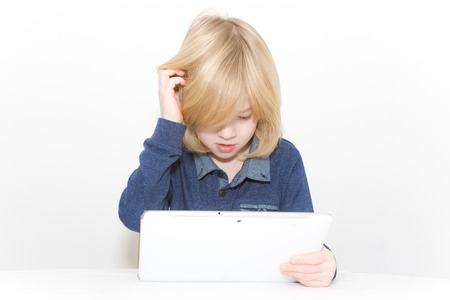 Young blonde boy playing on a tablet while scratching his headの写真素材