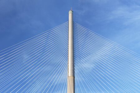 Rope and pylon of modern suspension bridge against blue sky. Building abstract background