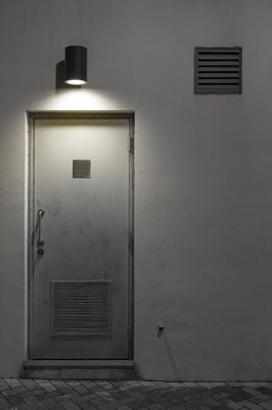 Light, air vent and door on wall at nightの写真素材