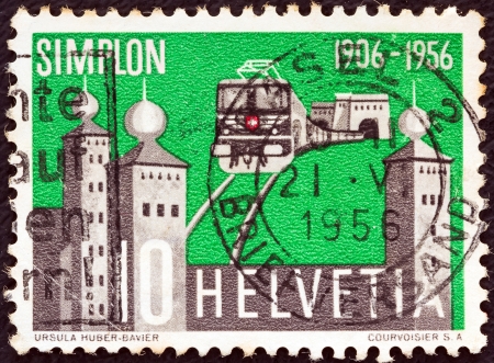 SWITZERLAND - CIRCA 1956: A stamp printed in Switzerland issued for the 50th anniversary of opening of Simplon Tunnel shows electric train emerging from the tunnel and Stockalper Palace, circa 1956. のeditorial素材
