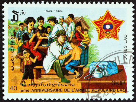 LAOS - CIRCA 1989: A stamp printed in Laos from the \"40th anniversary of People\'s Army \" issue shows Army medics vaccinating civilians, circa 1989.のeditorial素材