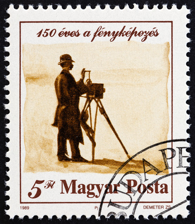 HUNGARY - CIRCA 1989: A stamp printed in Hungary issued for the 150th anniversary of photography shows photographer with camera, circa 1989.のeditorial素材