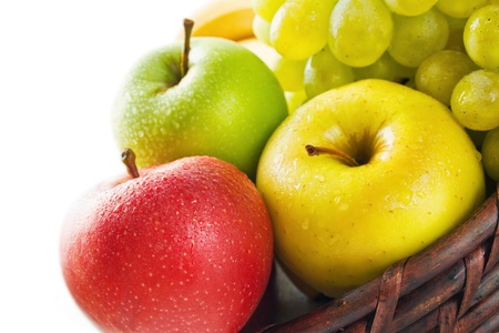 Fruits. Three apples in different colors placed in a wicker basket with some grape and banana isolated on whiteの写真素材