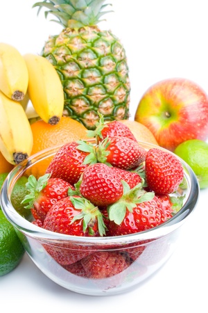 	Fruits. Arrangement of various fresh ripe fruits: pineapple, bananas, oranges, apple, limes and strawberries in a glass bowl closeup isolated on white background.の写真素材