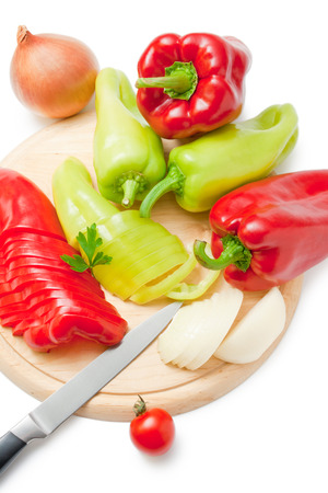 Fresh ripe red and green peppers and onions placed on a wooden cutting board and around arranged with kitchen knife cherry tomato and parsley sprig isolated on white background.の写真素材