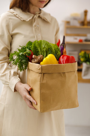 A young woman holds a bag of vegetables in the kitchenの写真素材