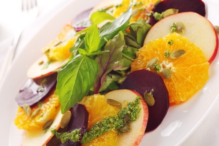 Fresh salad with beet, apple, orange and basil pesto dressing on white plate.の写真素材