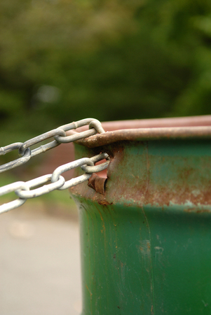 Image of a chained rusted garbage can in a park. Selective focus on where the chain is connected to the garbage can. Lots of space for content.の写真素材