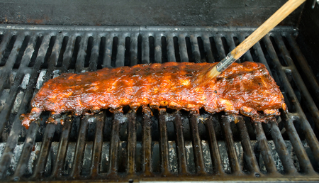 Brush slathering BBQ sauce on some tender baby back ribs. Shallow depth of field - focus at the end of the brush.の写真素材