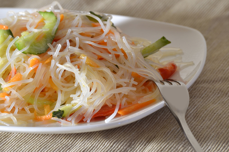 Funchoza salad with vegetables on a white plate with a forkの写真素材