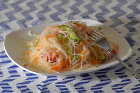 Funchoza salad with vegetables on a white plate with a forkの写真素材