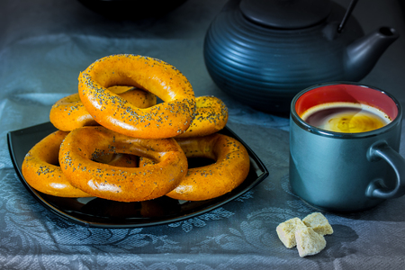 Black coffee cup with bagels on a black bowl and three pieces of sugar on a blue backgroundの写真素材