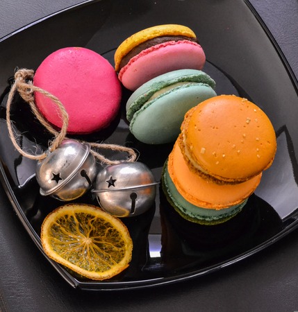 French macaroon pastry cookies (macarons, macaroni) on a black shiny plate with dried oranges and bellsの写真素材
