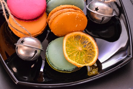French macaroon pastry cookies (macarons, macaroni) on a black shiny plate with dried oranges and bellsの写真素材