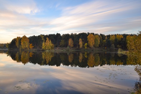 Dawn in the forest near the lake. The forest is reflected in the water. Autumn Early morning. Russia