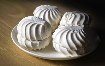 Marshmallow four delicious sweet desserts of white marshmallows zephyr on a plate in contrast lighting on a wooden table. Lack of coverage. Eveningの写真素材