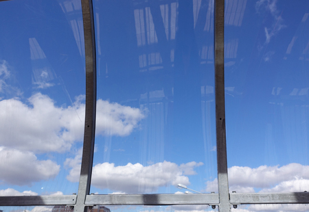 Blue sky with clouds behind curved glass.の写真素材