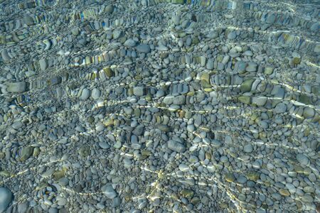 Stones in the sea water and ripples. Pebbles under water. Nautical background. Clean and transparent water. Mediterranean sea.の写真素材