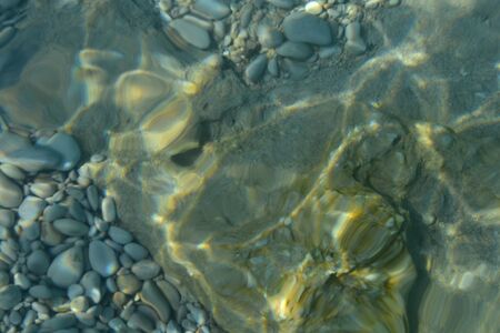 Top view of transparent clear water of river or creek with pebble stones. Abstract nature background