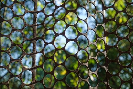 Fencing of a metal sheet with round holes against the blue sky.の写真素材