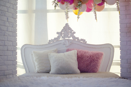 White bed with pillows, brick wall and flowersの写真素材