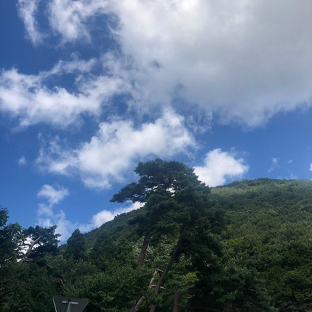 Beautiful view of a green mountain with blue sky and white cloudsの写真素材